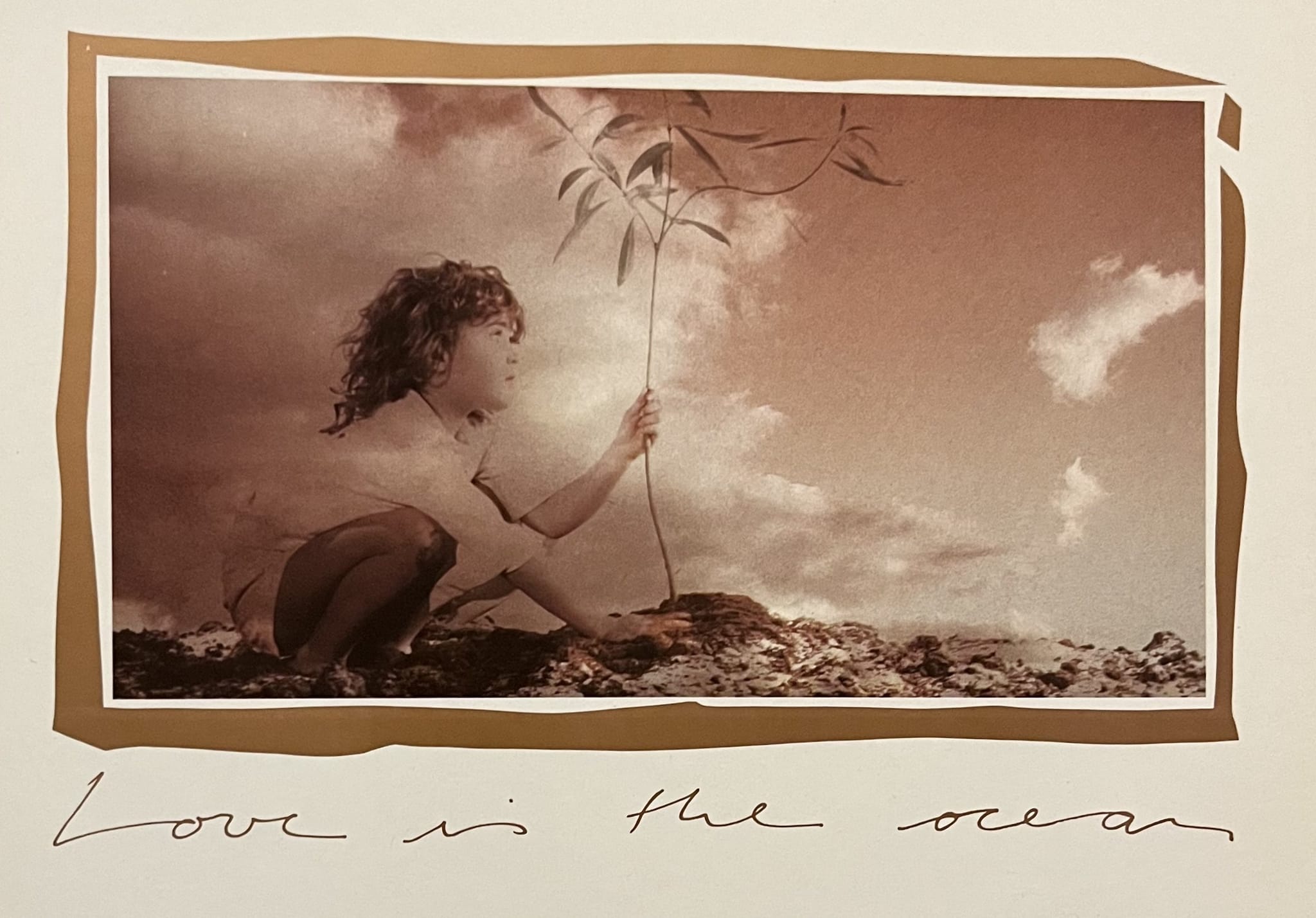 Sepiafarbenes Moodbild eines Kindes, das einen jungen Baum pflanzt, mit der handgeschriebenen Zeile „Love is the ocean“