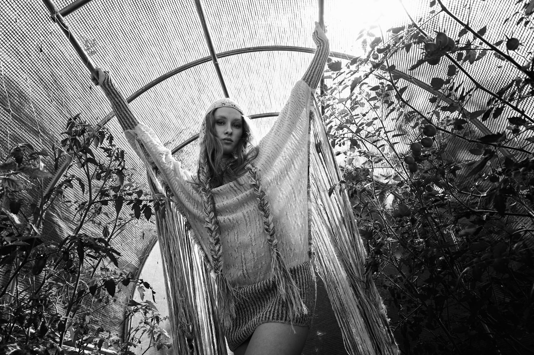 Schwarz-Weiß-Foto eines Models im Fransen-Strickkleid mit erhobenen Armen in einem Folientunnel